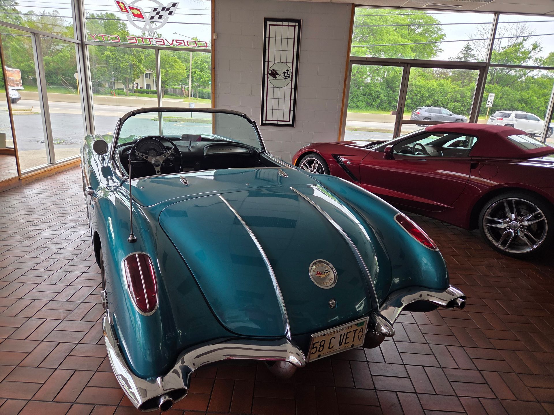Turquoise vintage convertible car displayed indoors next to a red sports car