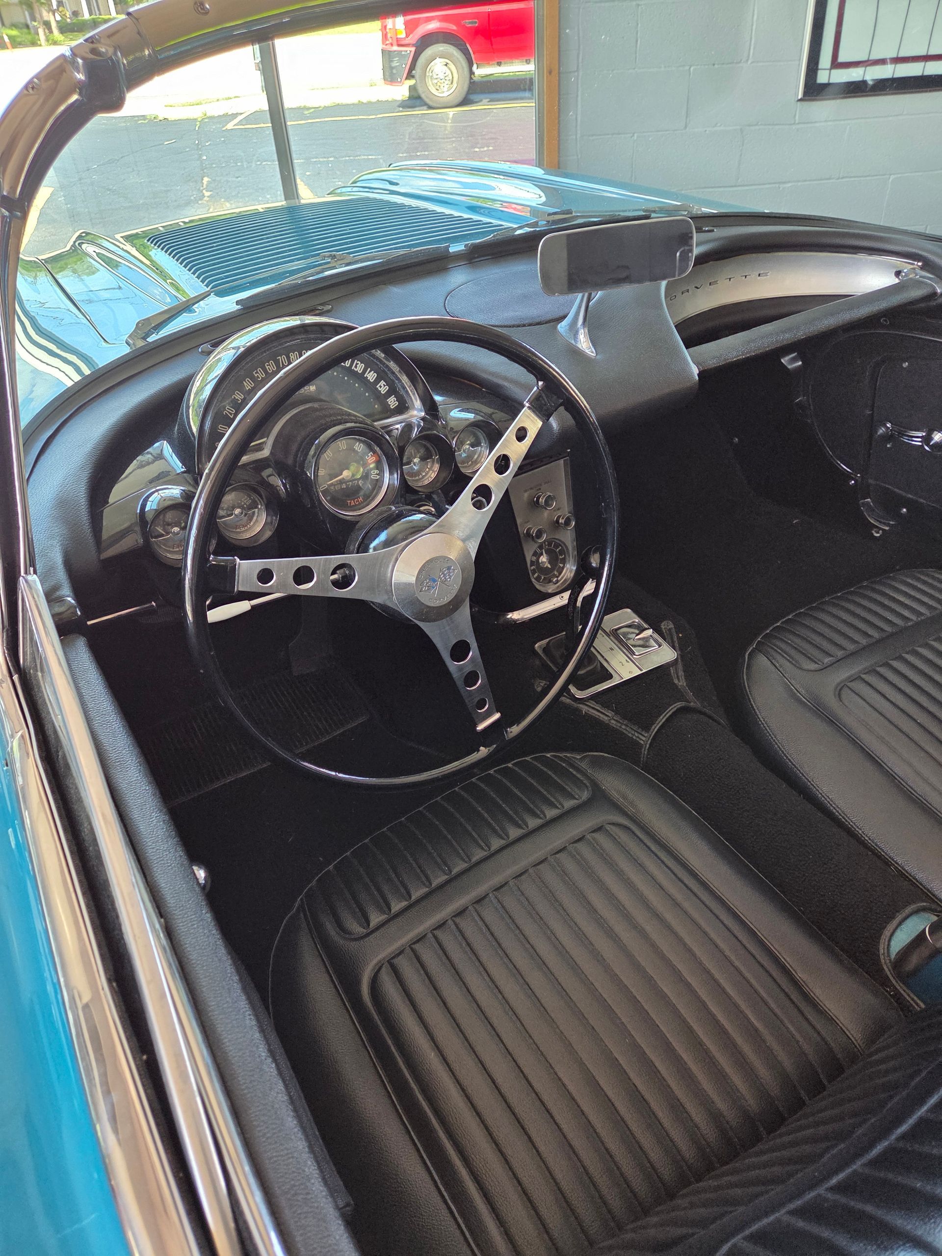 Vintage car interior with black bucket seats and a steering wheel, viewed from the open side door