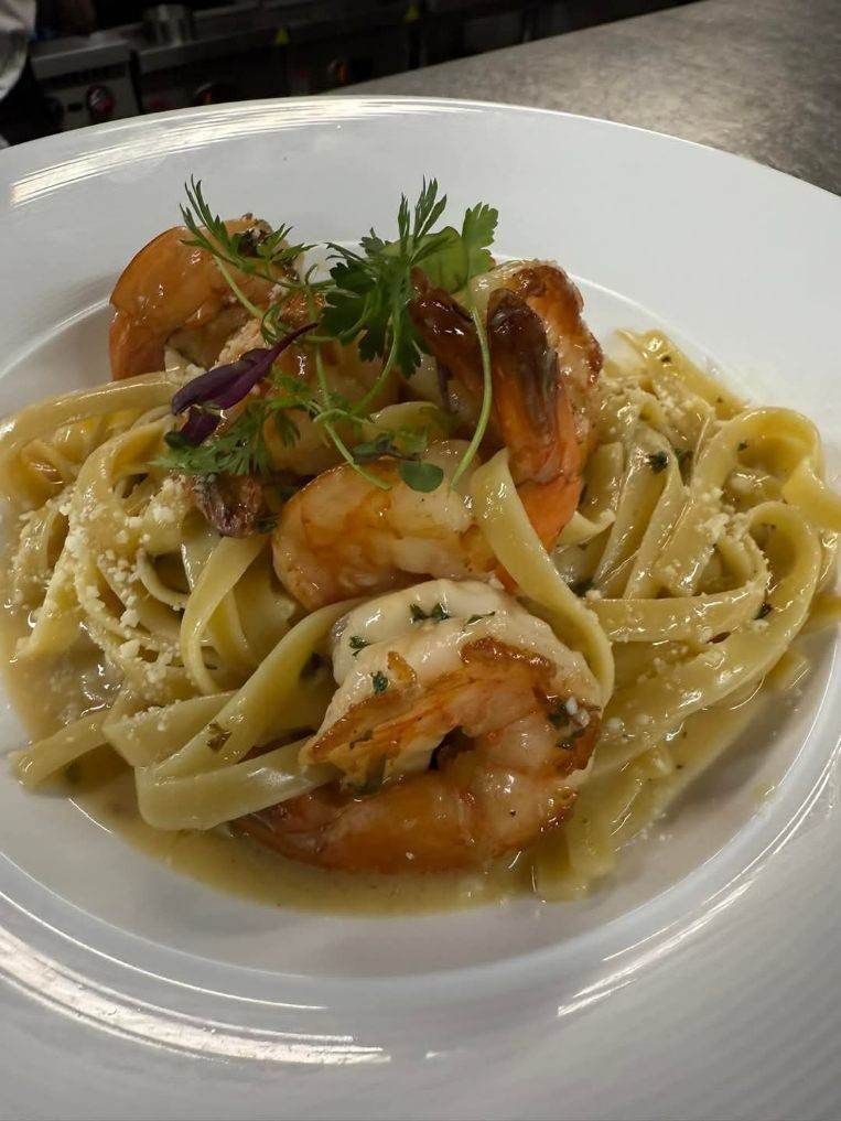 A white plate topped with pasta and shrimp on a table.