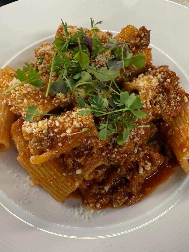 A close up of a plate of pasta with meat and sauce on a table.