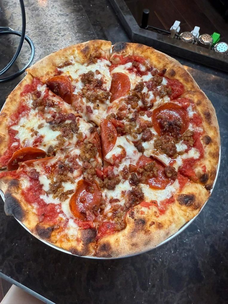 A pizza with pepperoni and sausage on a pan on a table.