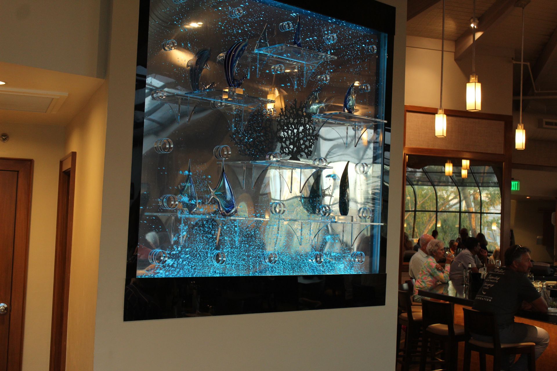 A large fish tank is hanging on a wall in a restaurant