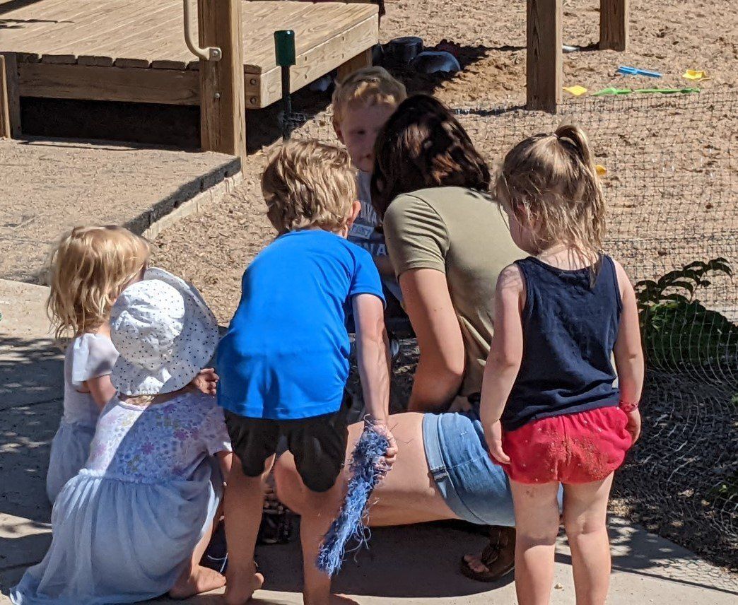 A woman is kneeling down with three children in a playground