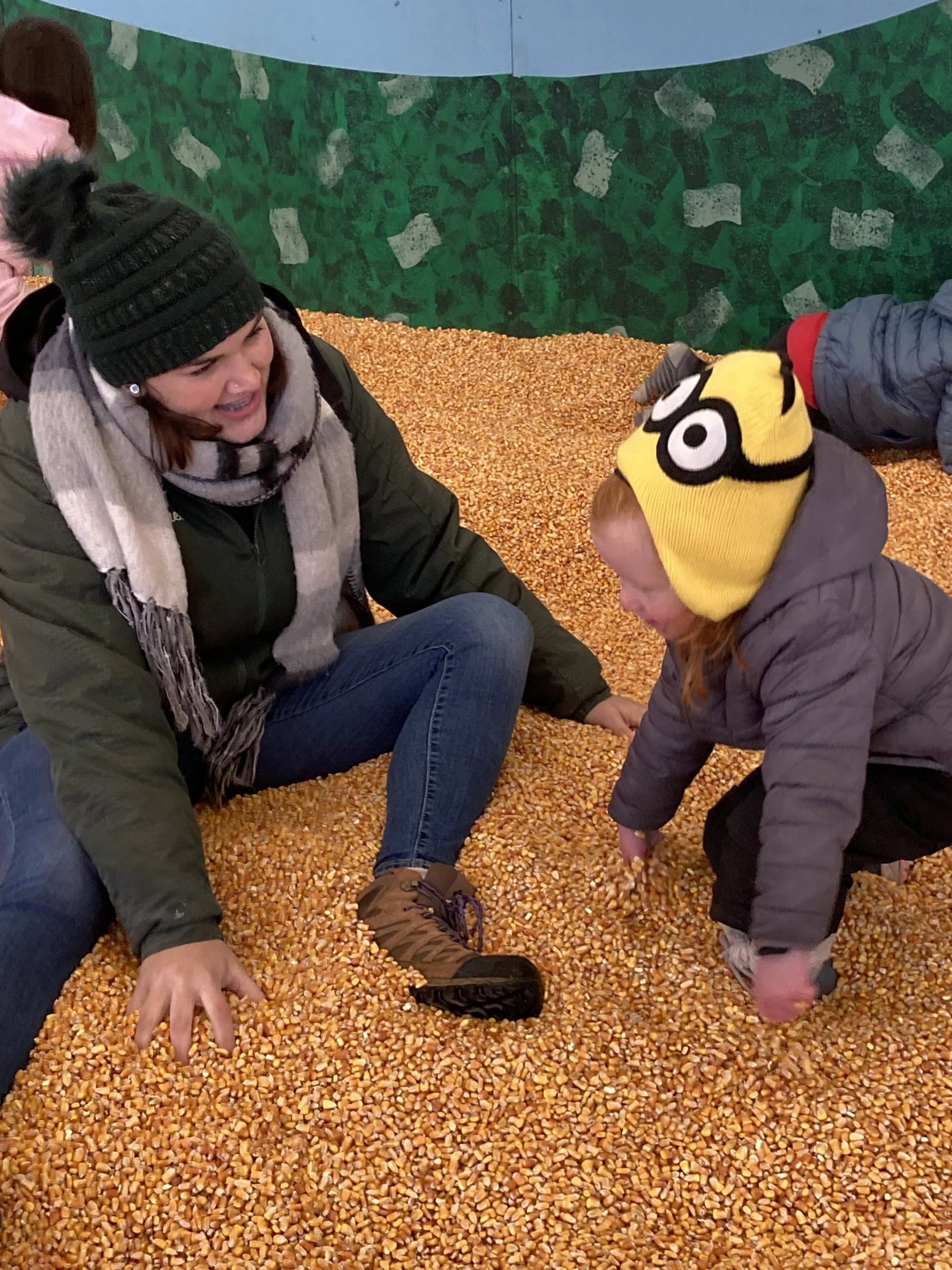 A woman and child are playing in a pile of corn