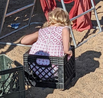 A little girl is sitting in a milk crate