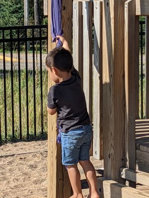 A young boy is climbing a wooden structure at a playground