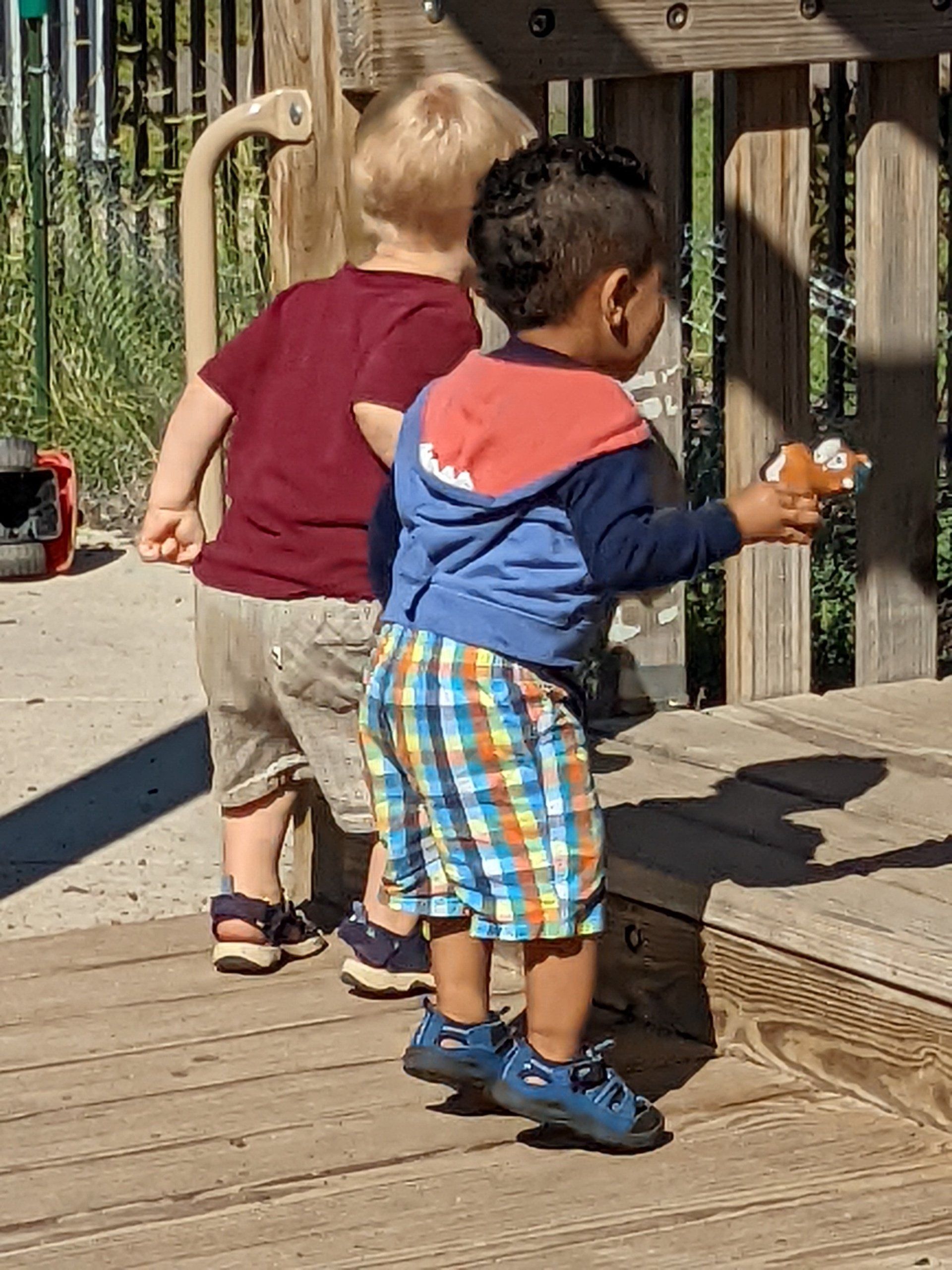 Two young boys are standing on a wooden deck 