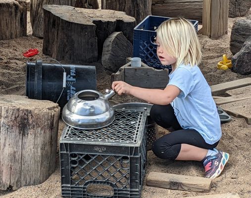A little girl playing with a tea kettle
