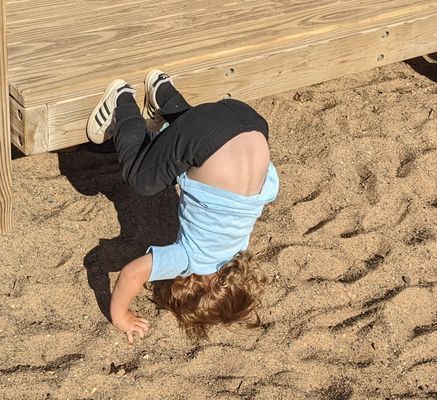A young boy is doing a handstand in the sand