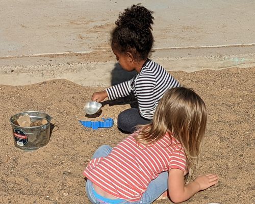 Two little girls are playing in the sand