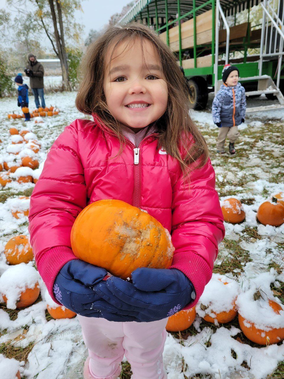A little girl in a pink jacket is holding a pumpkin 