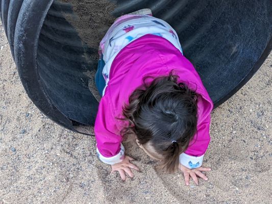 A little girl is crawling through a tunnel in the sand