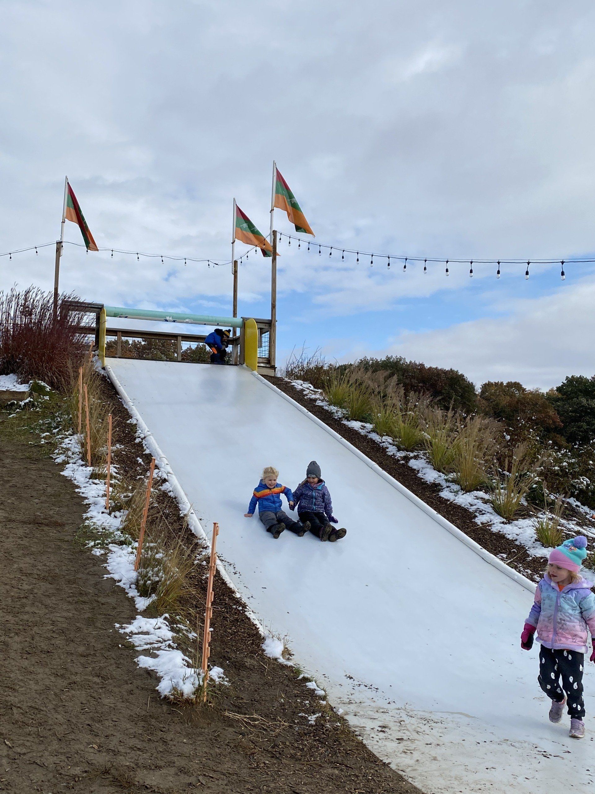 Two children are sliding down a snow slide