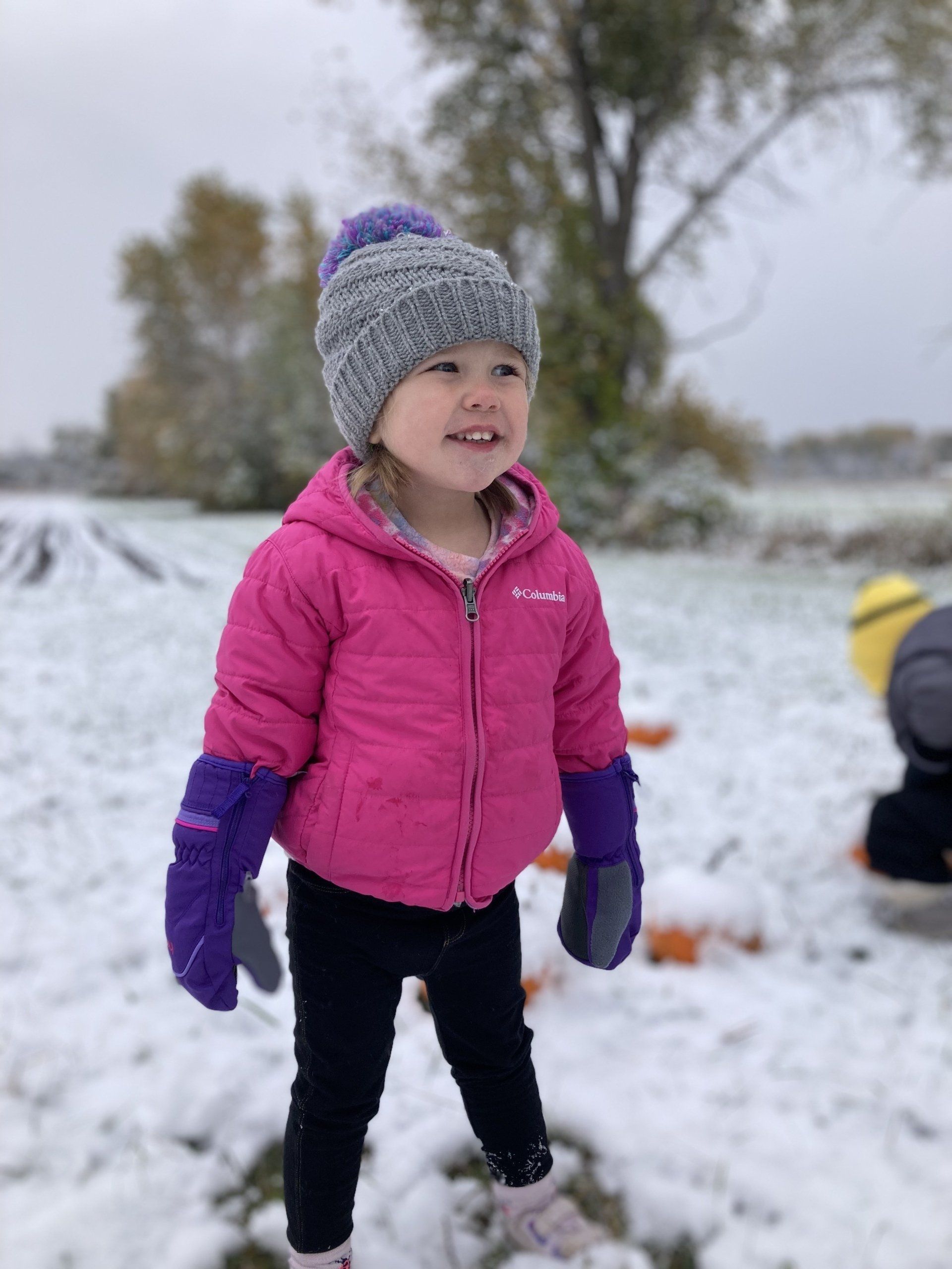 A little girl wearing a pink jacket and purple gloves