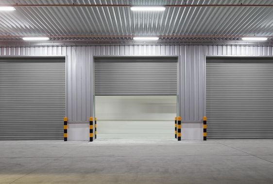 Empty industrial loading bay with three closed metal roll-up doors and striped safety posts