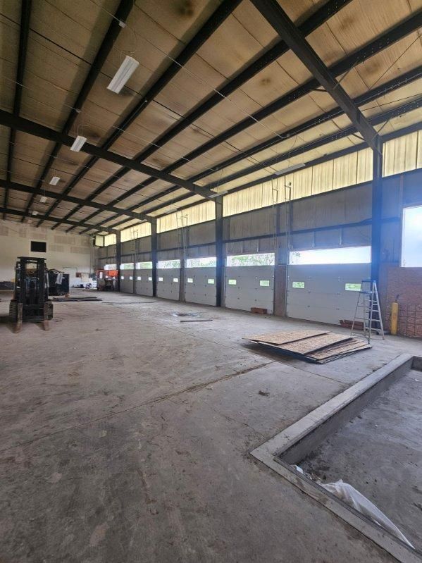 Empty industrial warehouse with high metal roof, concrete floor, and daylight through large side openings