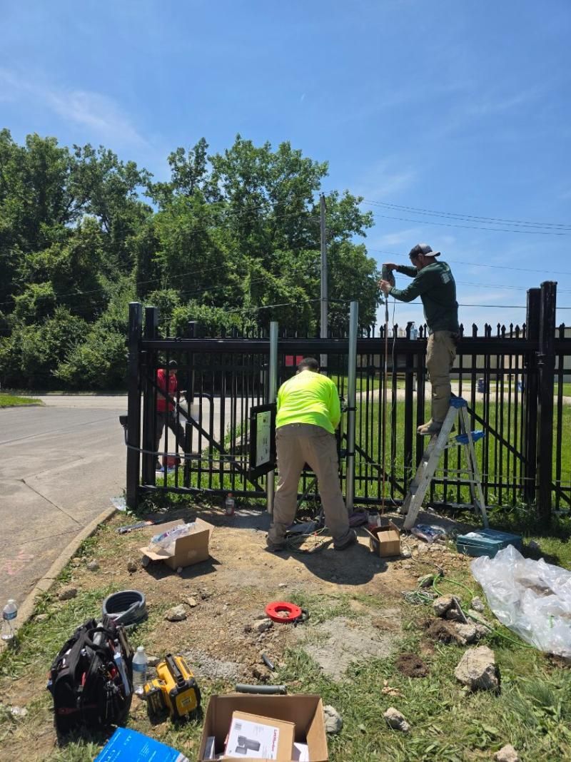 Workers repairing a black metal fence beside a road on a sunny day