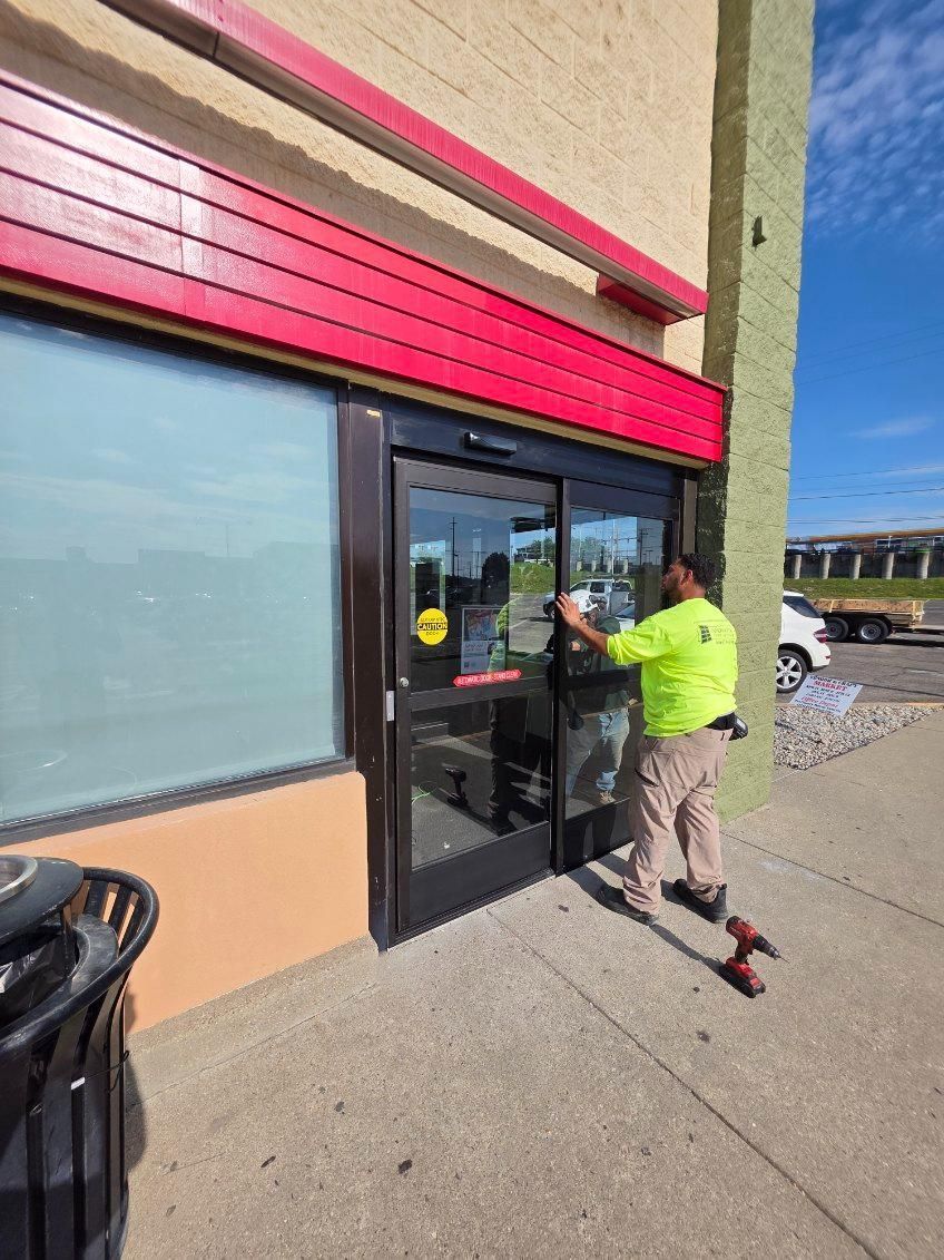 Person in neon jacket pushing open a glass storefront door on a sunny sidewalk.