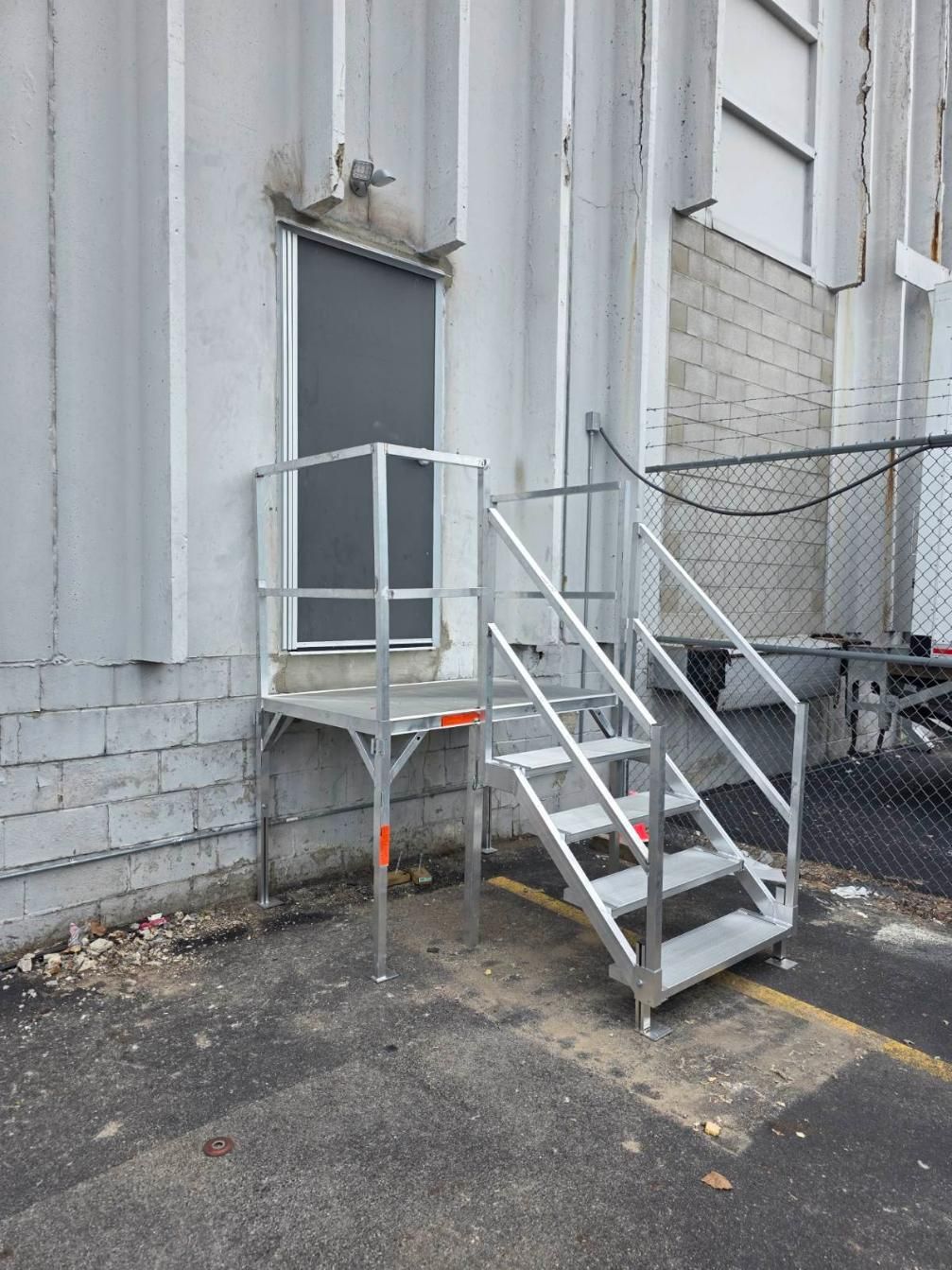 Metal platform and stairs leading to a side door on a gray industrial building.