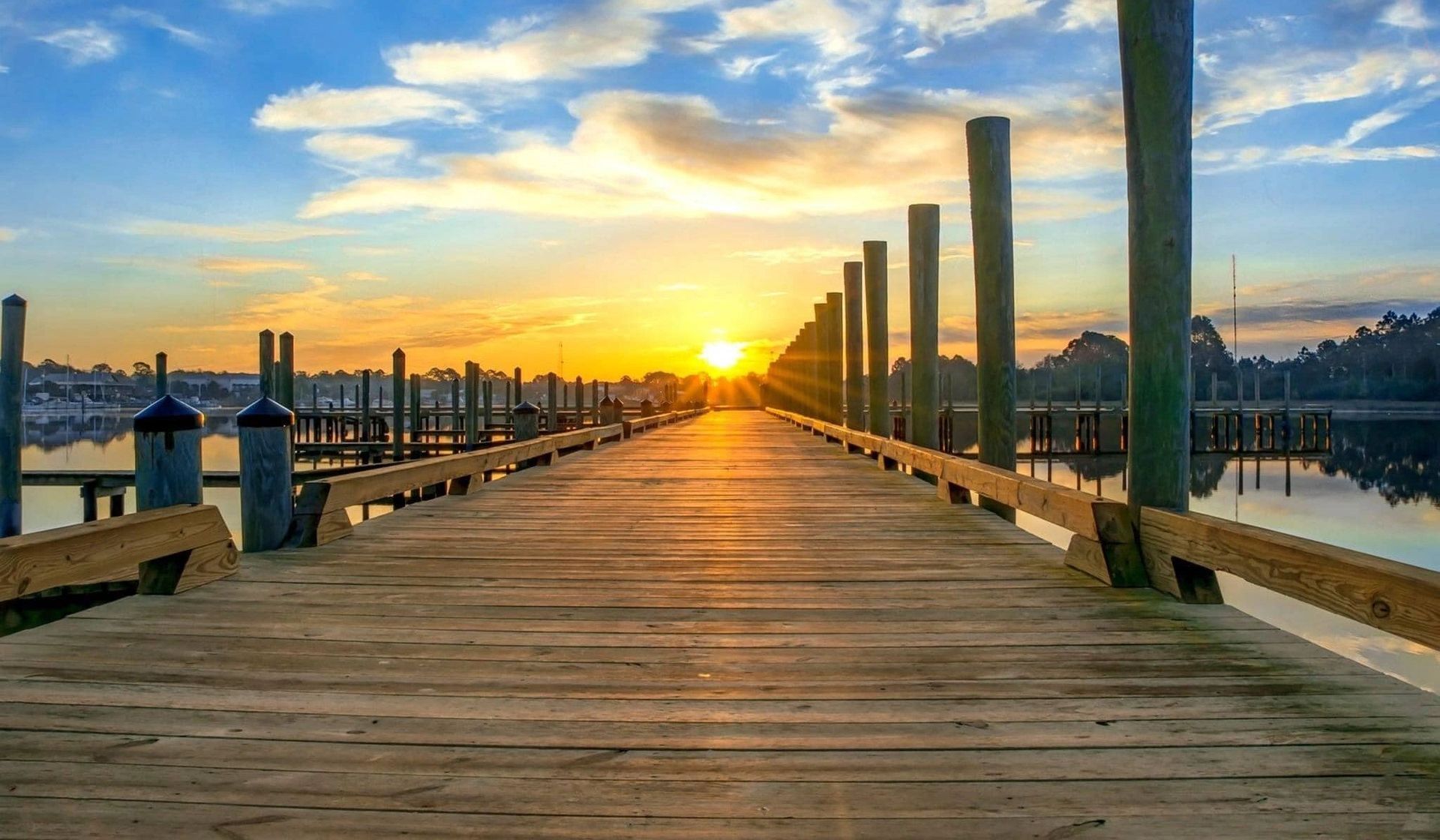A wooden dock leading to a body of water at sunset.