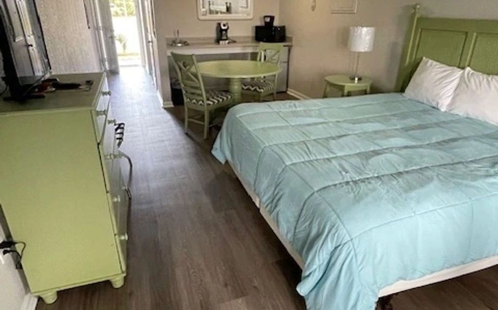 A hotel room with a bed , dresser , table and chairs.