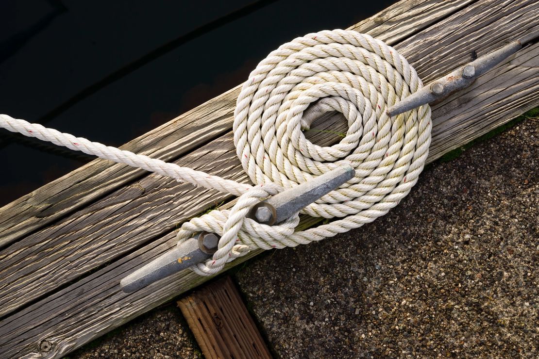 A white rope is tied to a wooden dock.