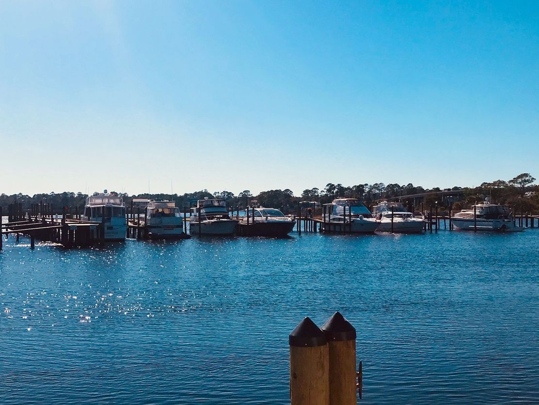 A row of boats are docked in a harbor on a sunny day.