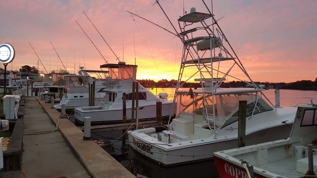 A group of boats are docked at a marina at sunset.