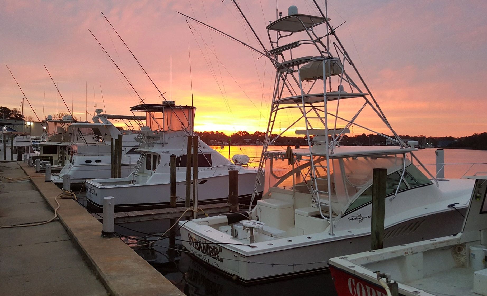 A group of boats are docked at a marina at sunset.