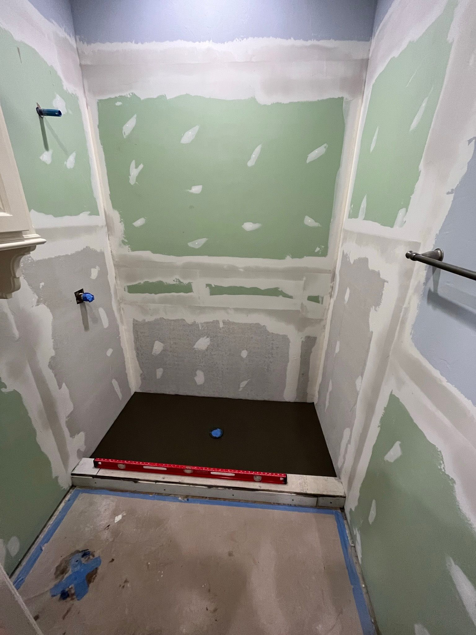 Shower under construction with green wallboard, dark brown floor, and tools.