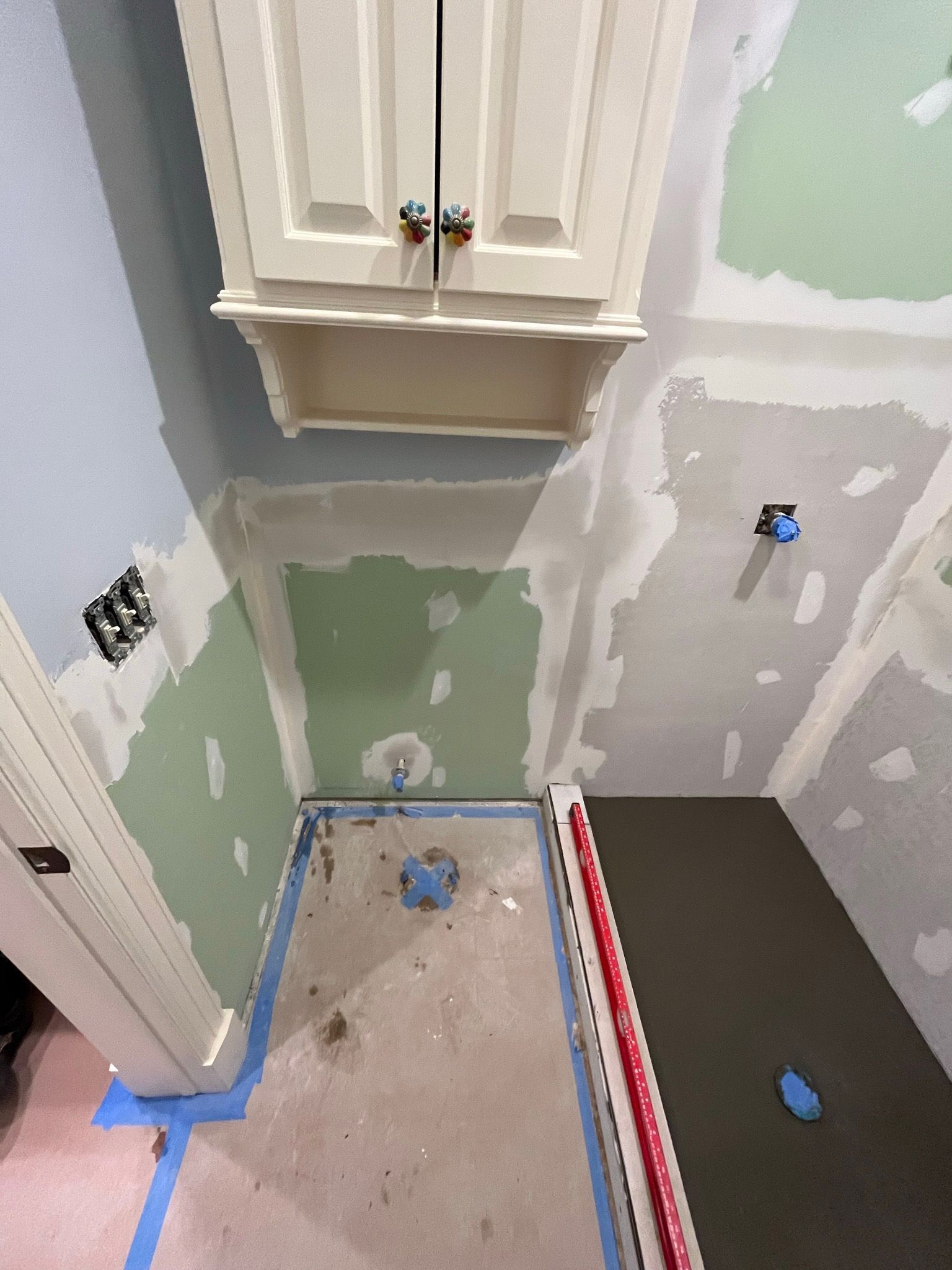 Bathroom remodel with unfinished walls, cabinet, shower base, and blue tape.