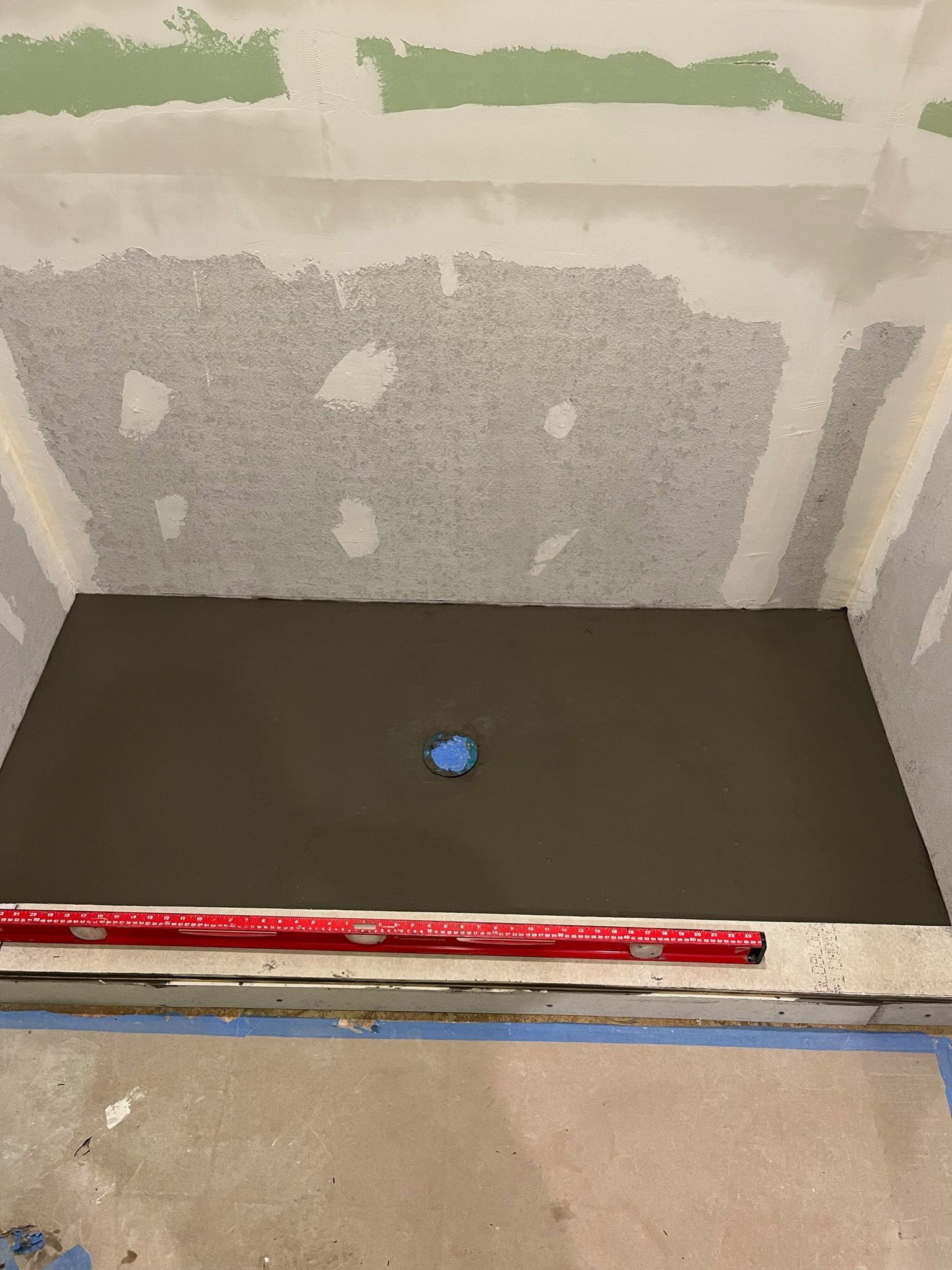 Newly poured shower pan with blue drain, red level, and unfinished walls.