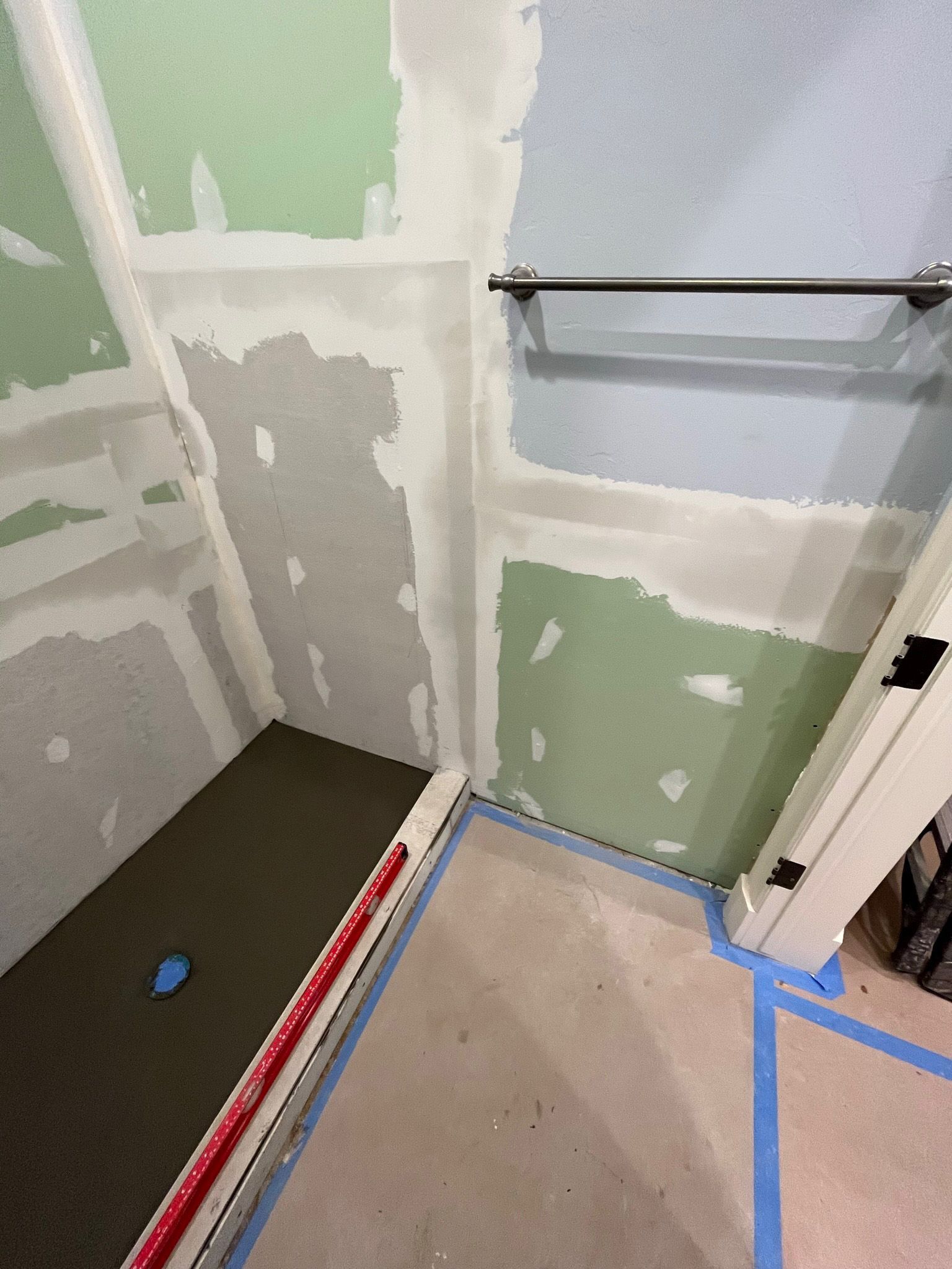 Bathroom under construction, green and white drywall, cement floor. A shower base and towel rack are visible.