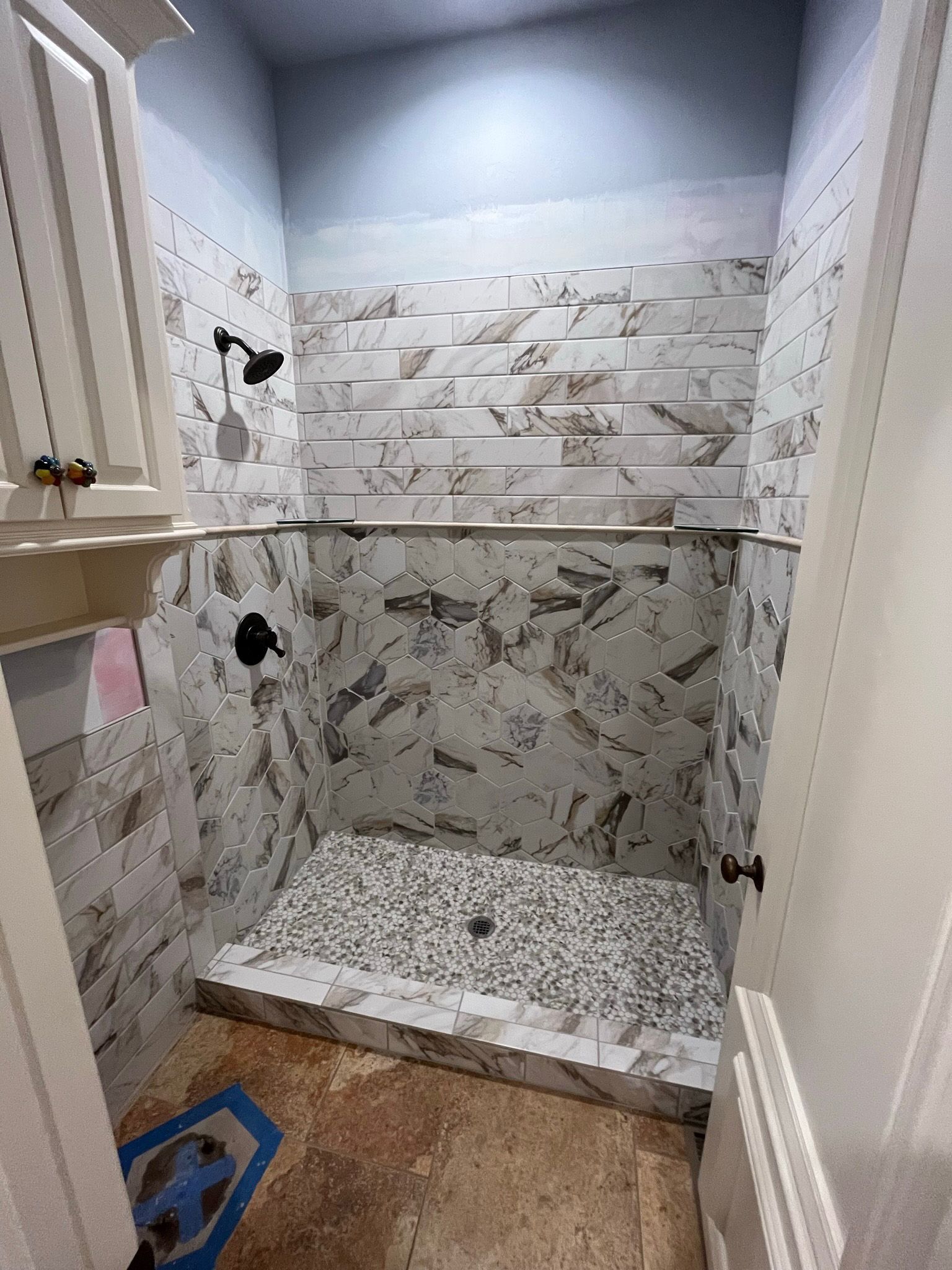 Shower with stone tile and black fixtures. Pebble shower floor and tiled walls.