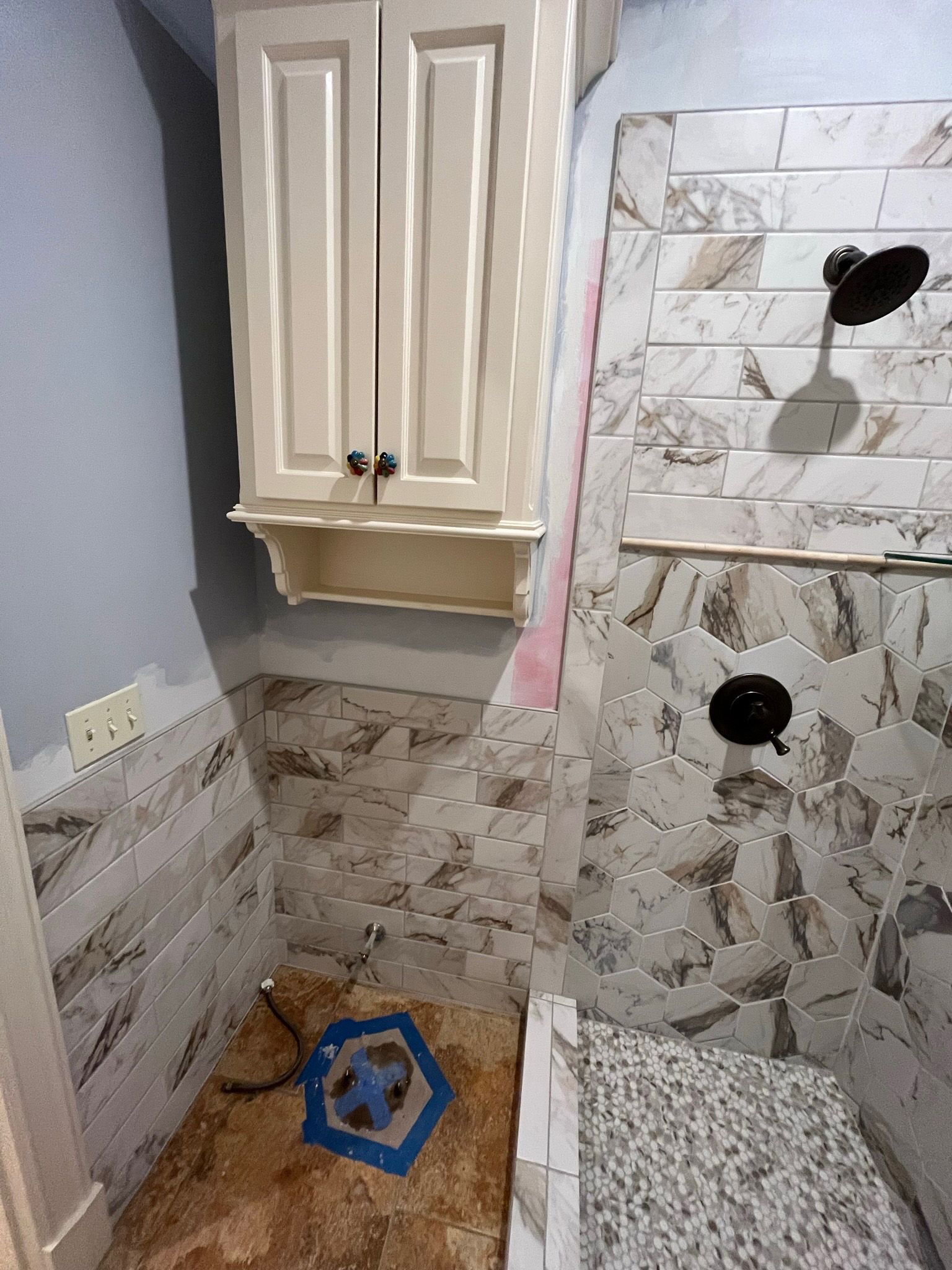 Bathroom renovation with new tile and shower fixtures; wall cabinet, open shower, blue fan.