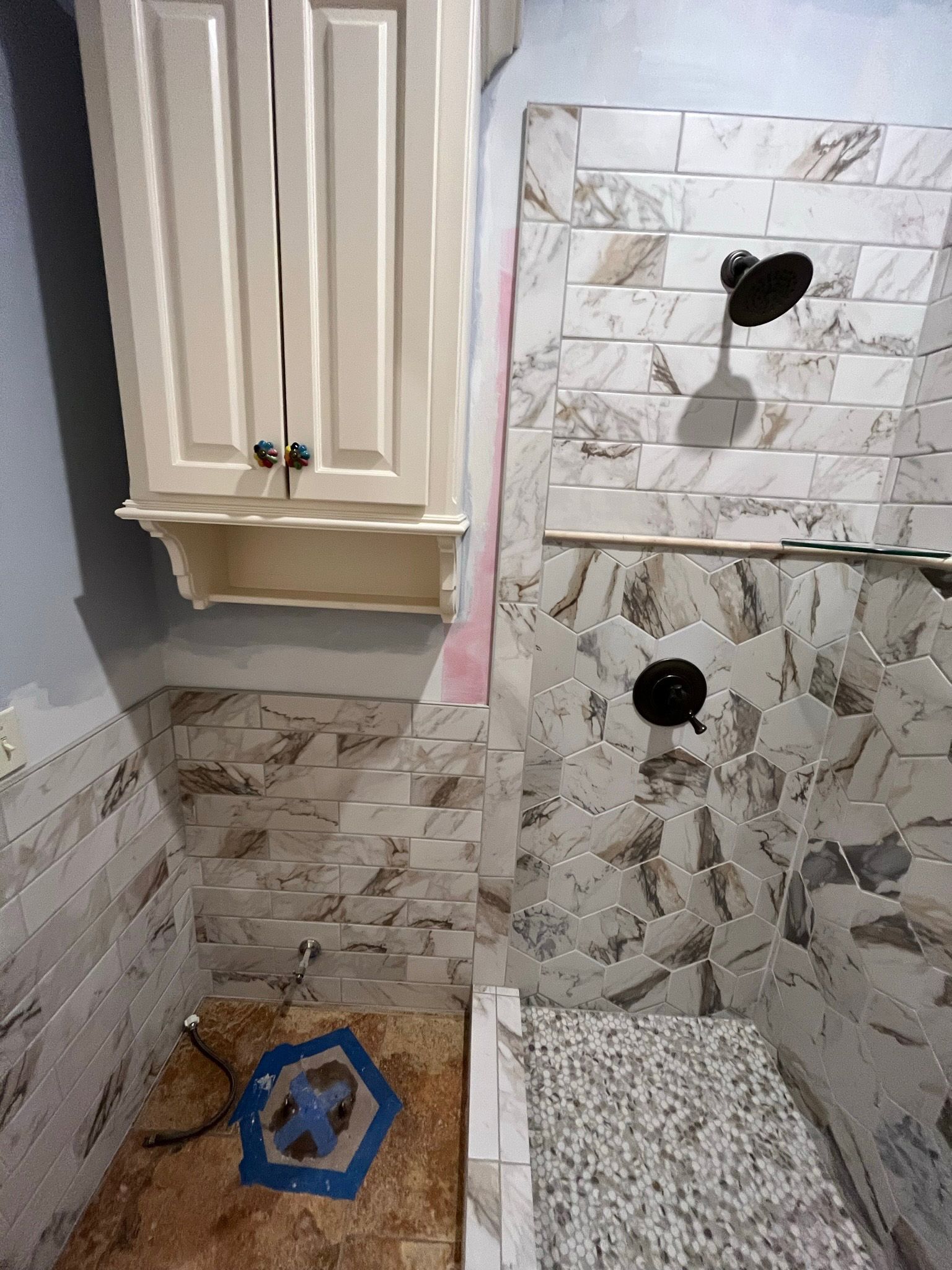 Shower under construction: tile walls, cabinet, shower head, and floor.