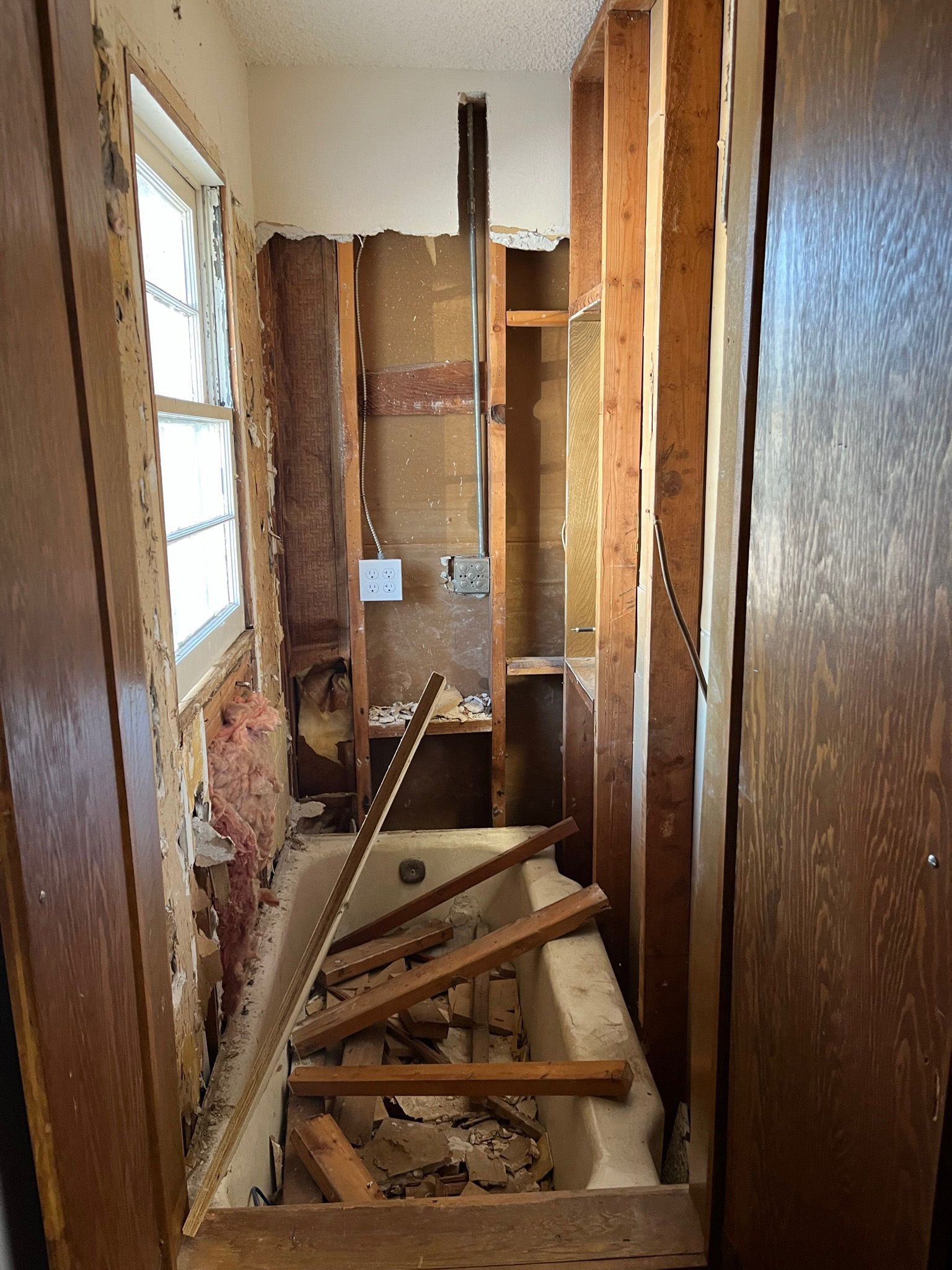 Bathroom renovation in progress; exposed studs, tub, and debris.