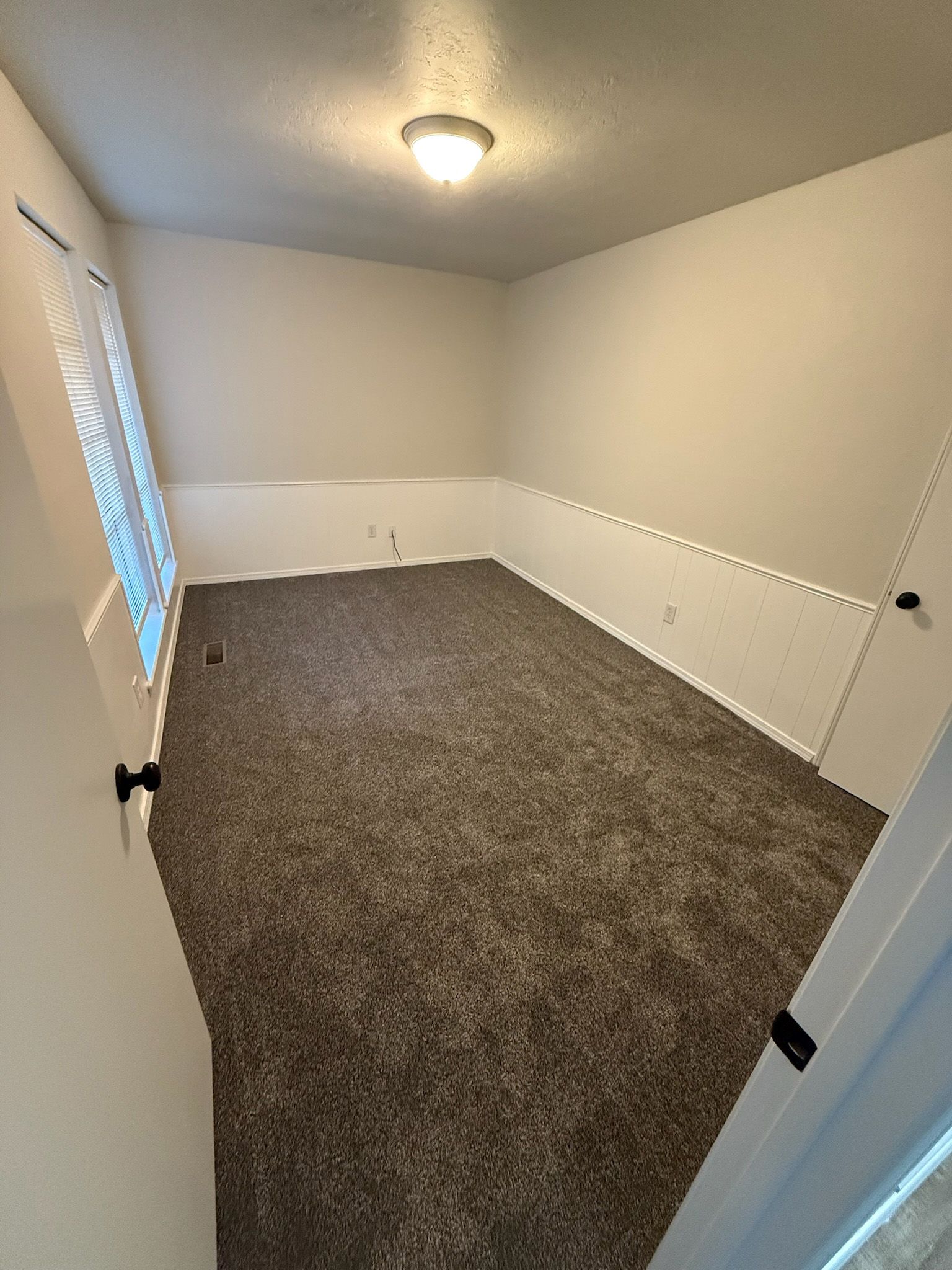 Empty room with brown carpet, white walls and trim, small window.