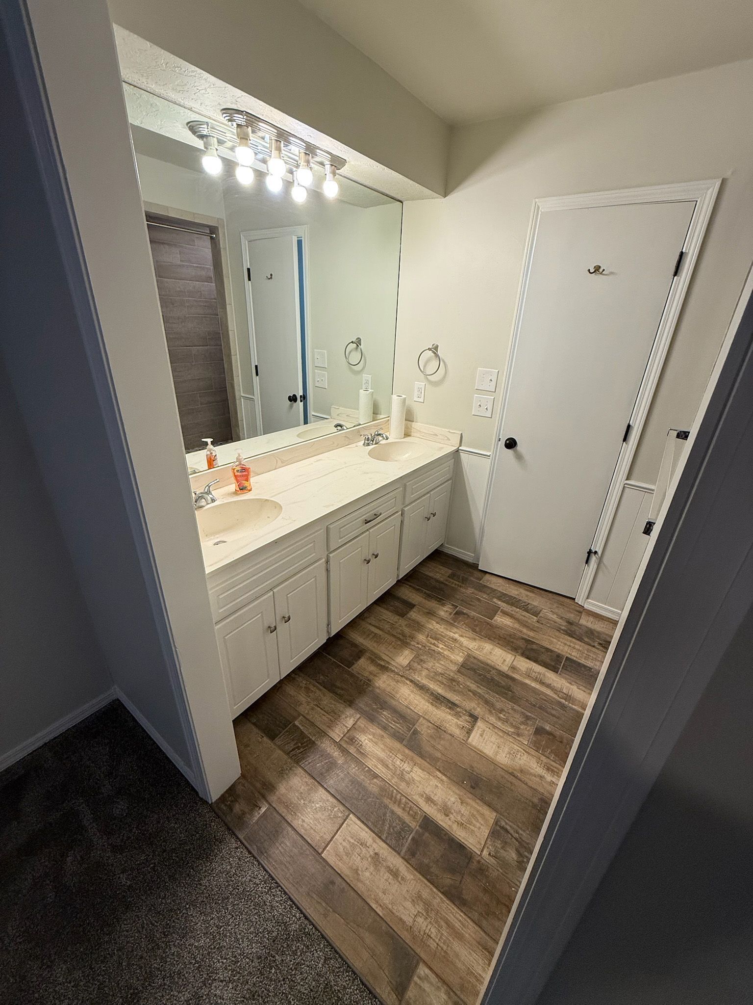 Bathroom with white cabinets, mirror, and wood-look flooring. Includes a closed white door.