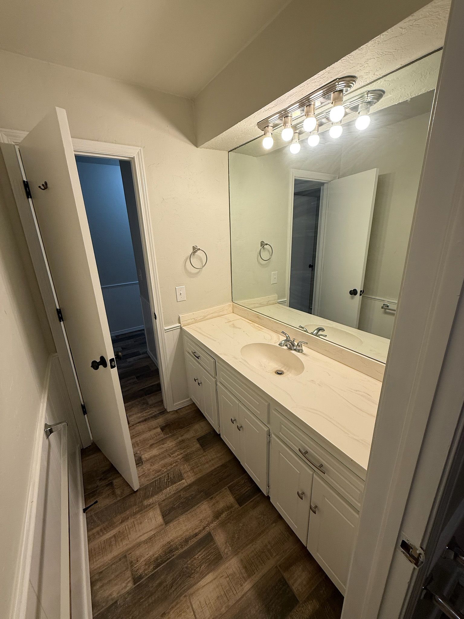 Bathroom with long vanity, large mirror, white cabinets, and open door to a small room.