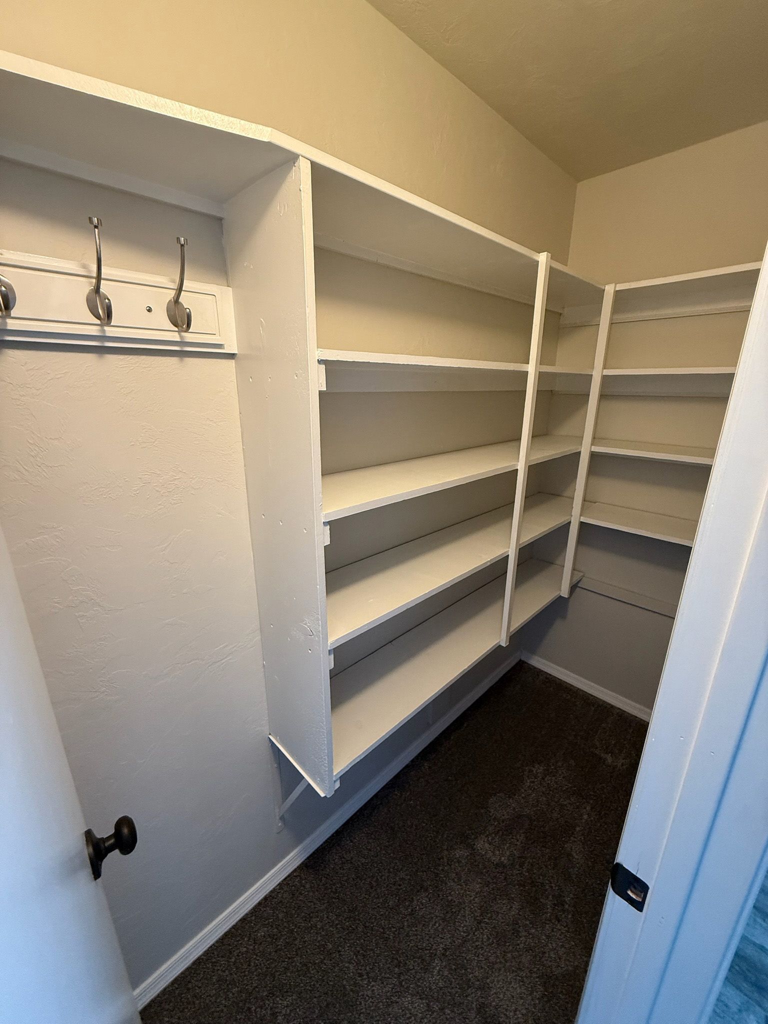 White pantry shelves and hooks, corner arrangement, carpeted floor.
