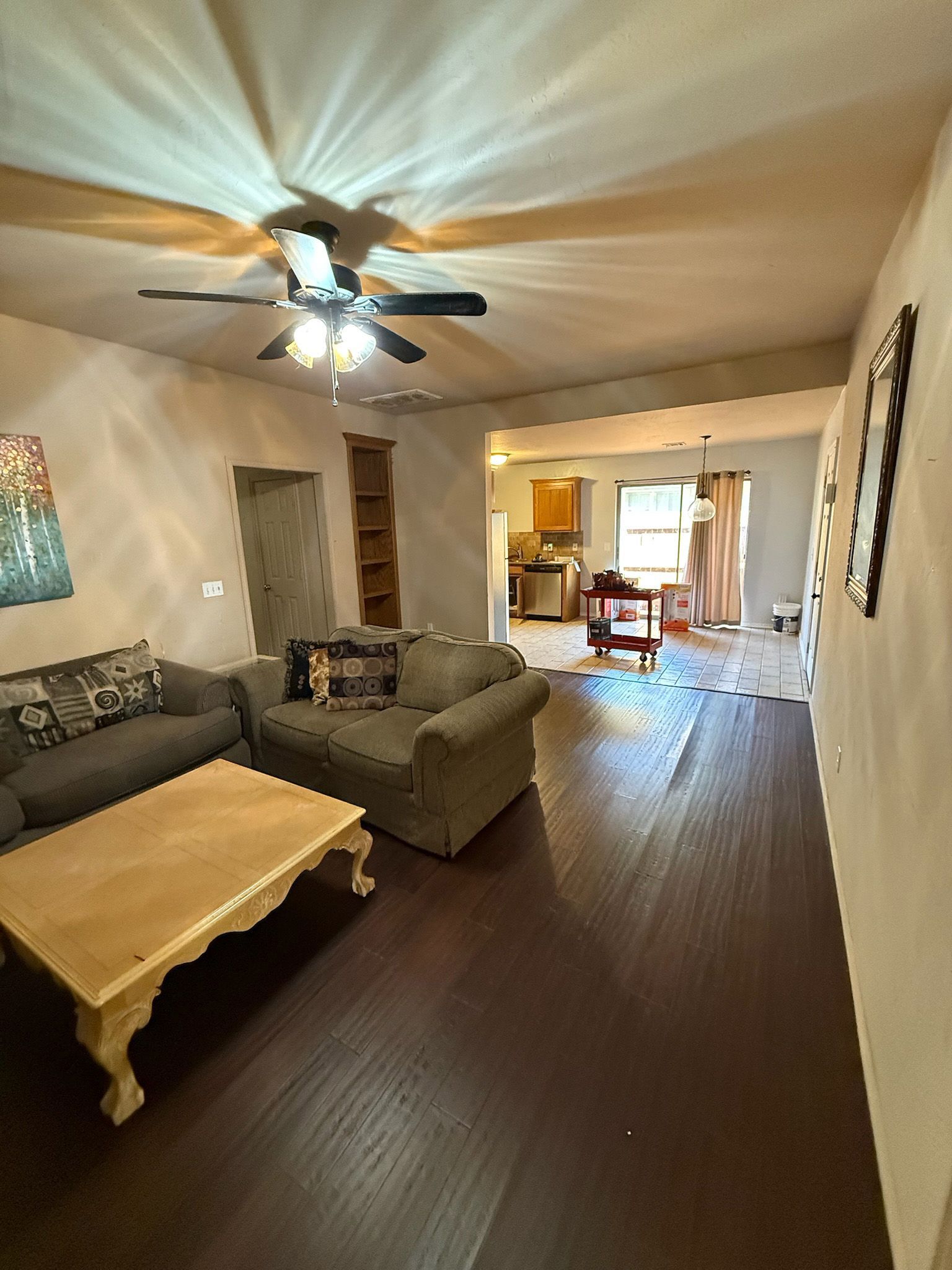 Living room with dark wood floors, two sofas, coffee table, and view into the kitchen.