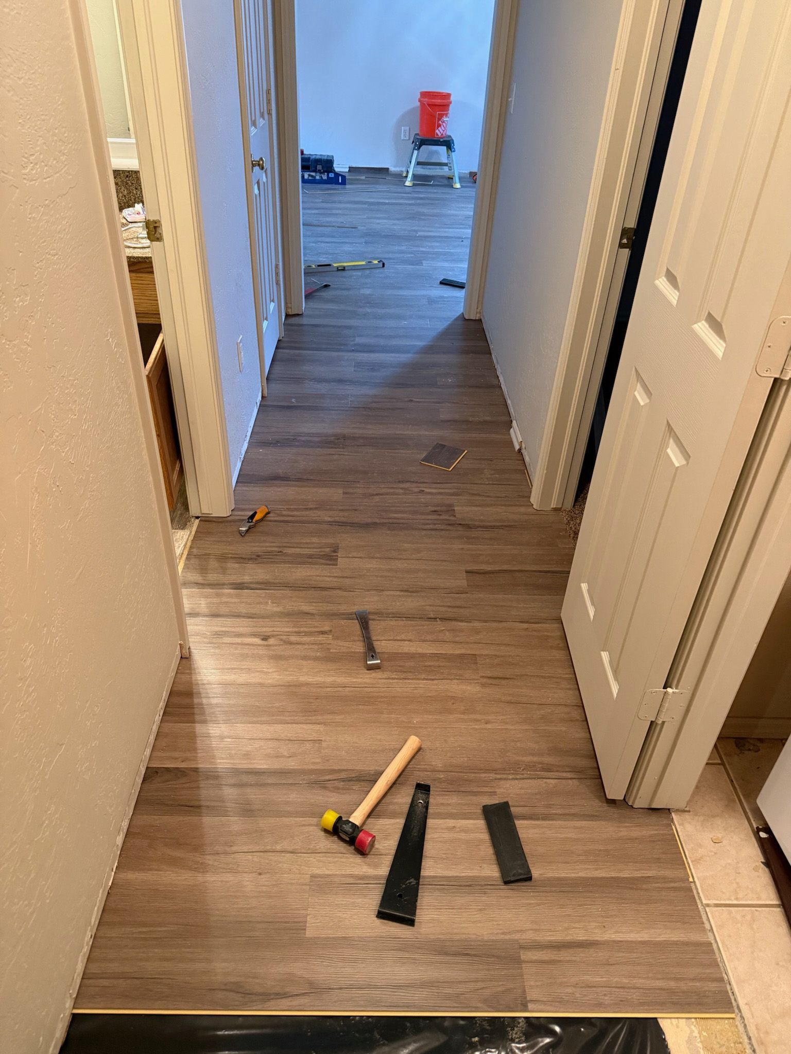 Hallway with wood-look flooring under installation; tools scattered about, doors on either side, unfinished wall to the left.