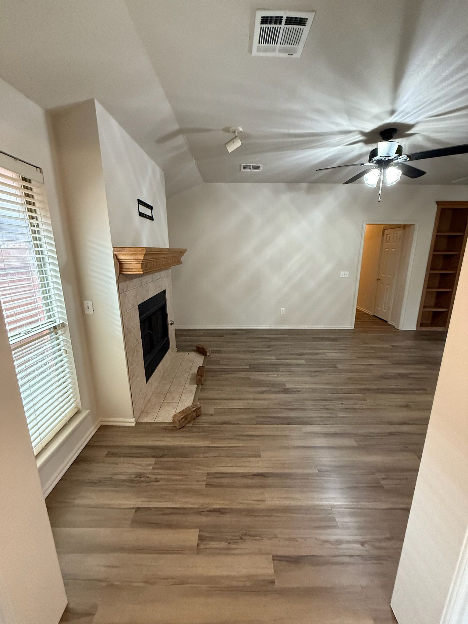 Living room with fireplace, wood floors, light walls. Ceiling fans and built-in shelves are visible.
