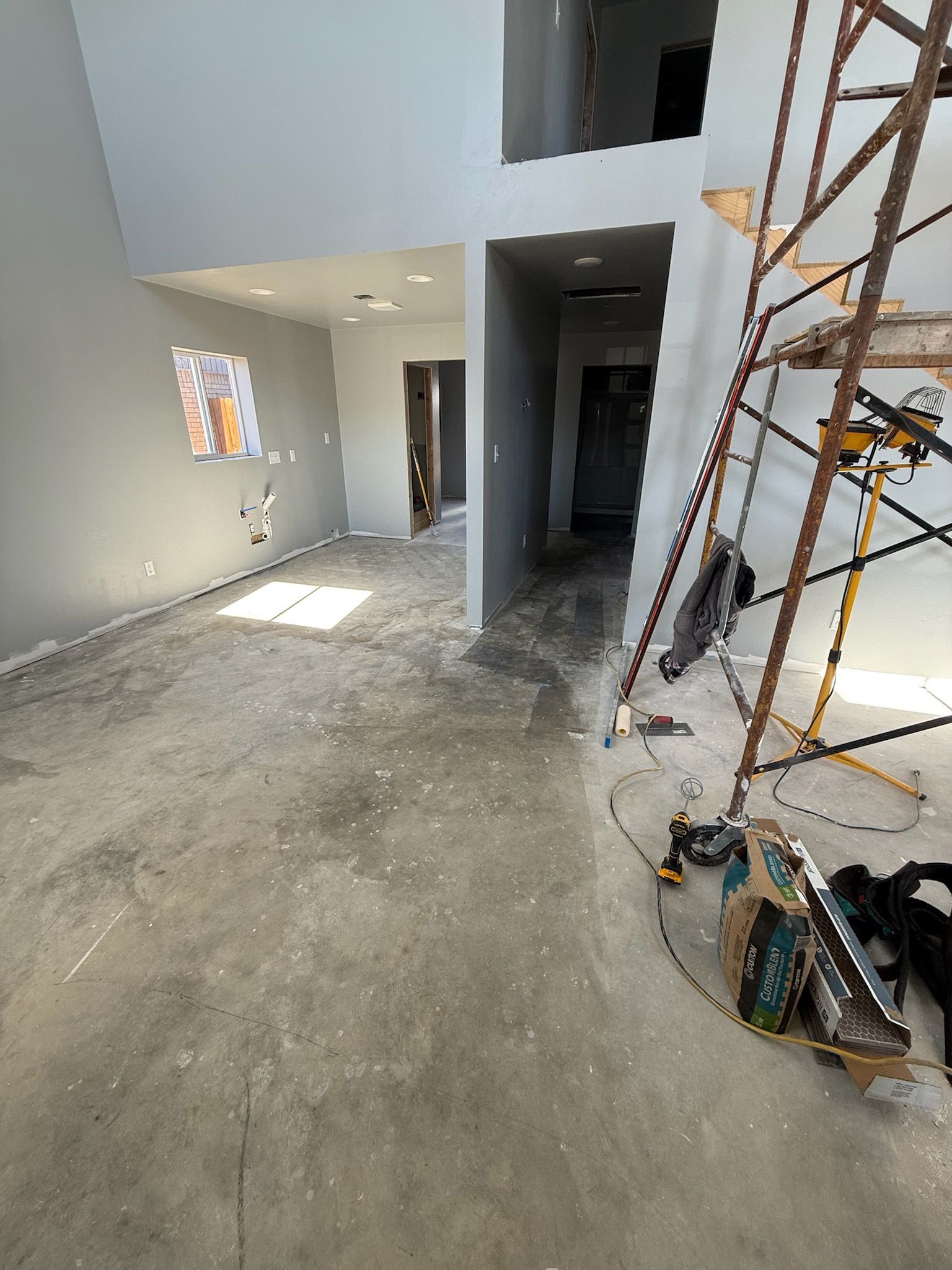 Interior under construction with gray walls, a ladder, and tools scattered on the floor.