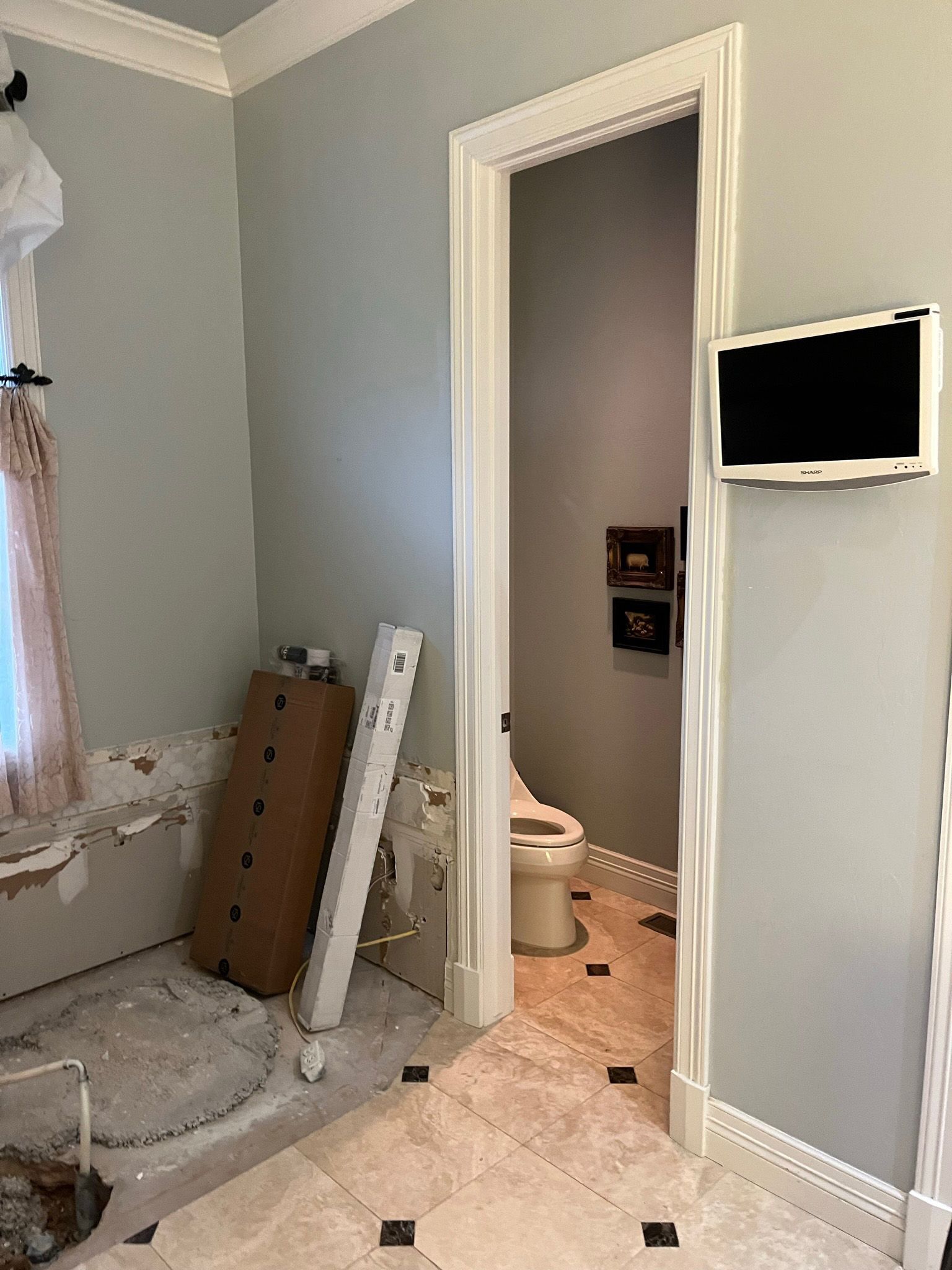 Bathroom with damaged walls, toilet, TV, and open doorway to another room.