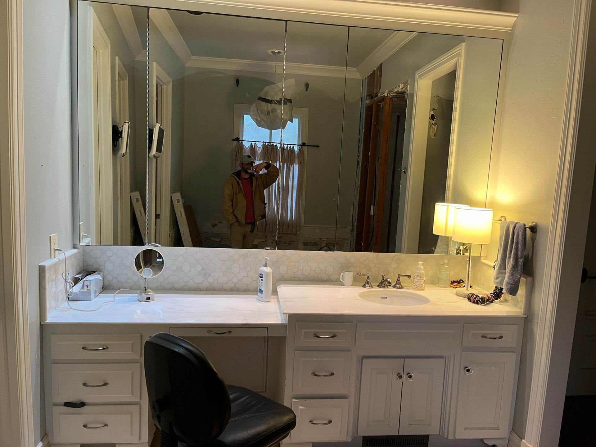 Vanity area with large mirror, white cabinets, white countertops, and a black chair.