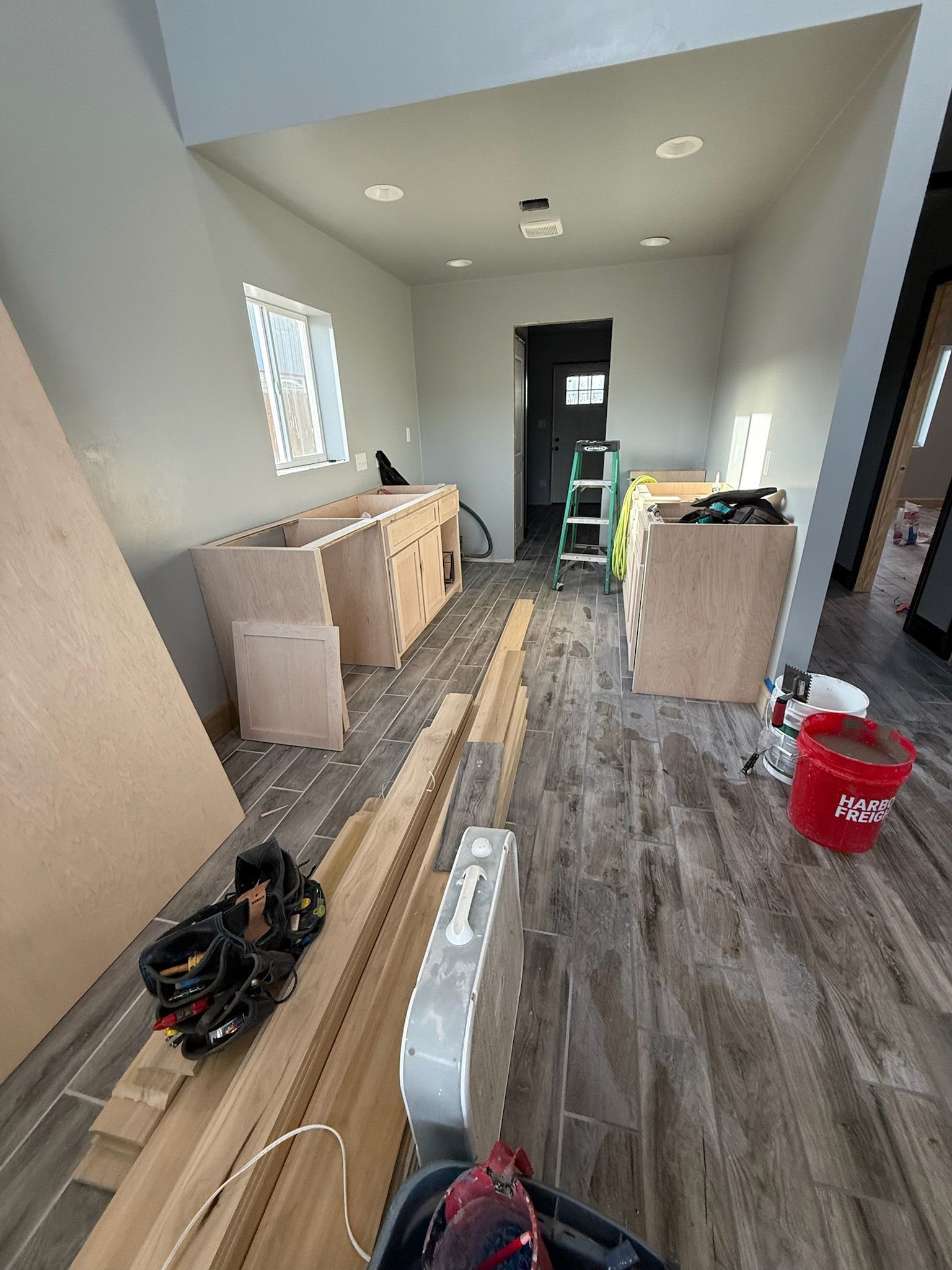 Kitchen under construction: cabinets, unfinished wood floors, tools, walls are gray, red bucket.