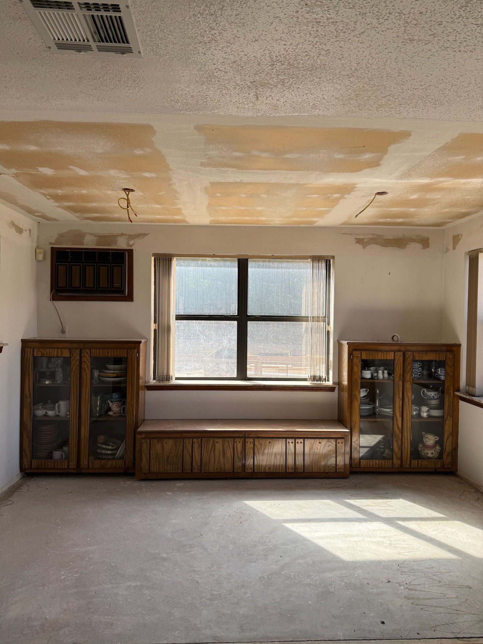 Empty room with wood cabinets flanking a window, window seat beneath. Ceiling damage.