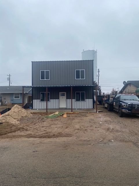 Two-story gray and white metal building with covered porch; dirt lot in front.